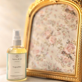 A bottle of 'Tropical Bliss' spray next to a decorative mirror with floral design on a light background.