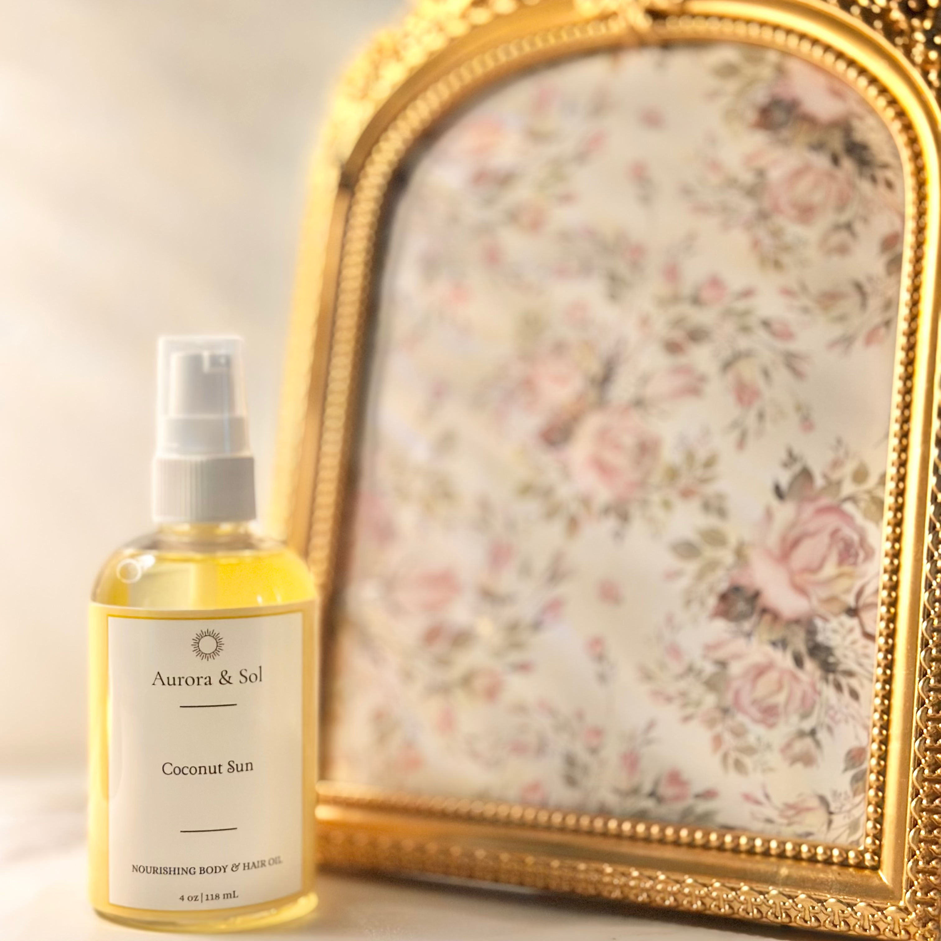 A bottle of Aurora & Sol coconut sun spray next to a decorative gold-framed mirror with floral design.